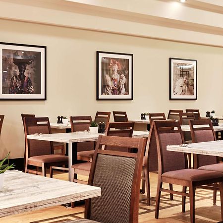 Radisson Blu Hotel Krakow Exterior photo The image shows a restaurant interior featuring a series of tables and chairs arranged neatly. The tables have a simple, modern design with light-colored surfaces. Brown chairs are set around the tables, some with dark cushions. The walls are decorat