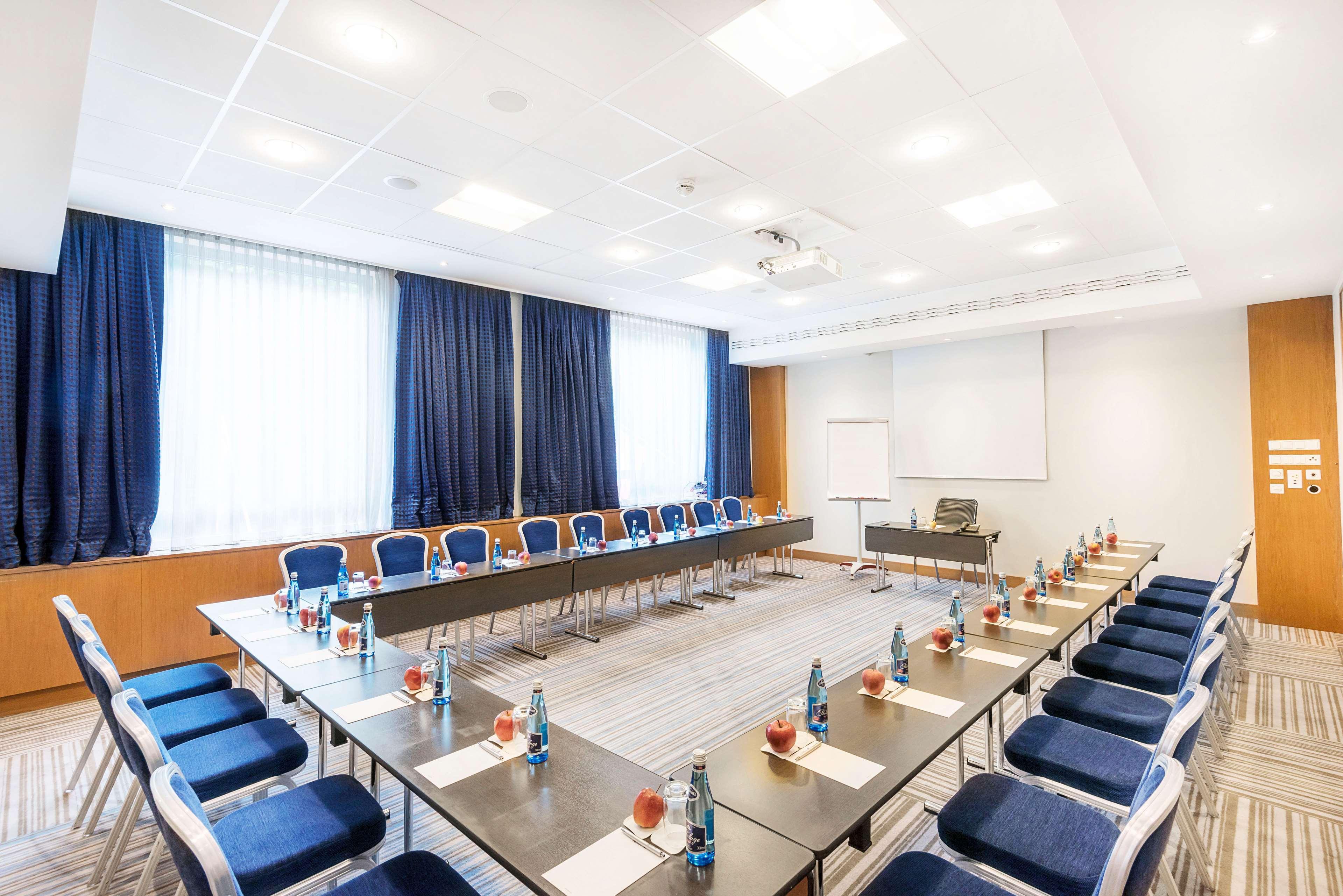 Radisson Blu Hotel Krakow Exterior photo The photo shows a modern conference room arranged for a meeting. In the center, there is a long rectangular table surrounded by chairs. Each place at the table has a small water bottle and what appears to be a notepad or menu. The room is well-lit wi