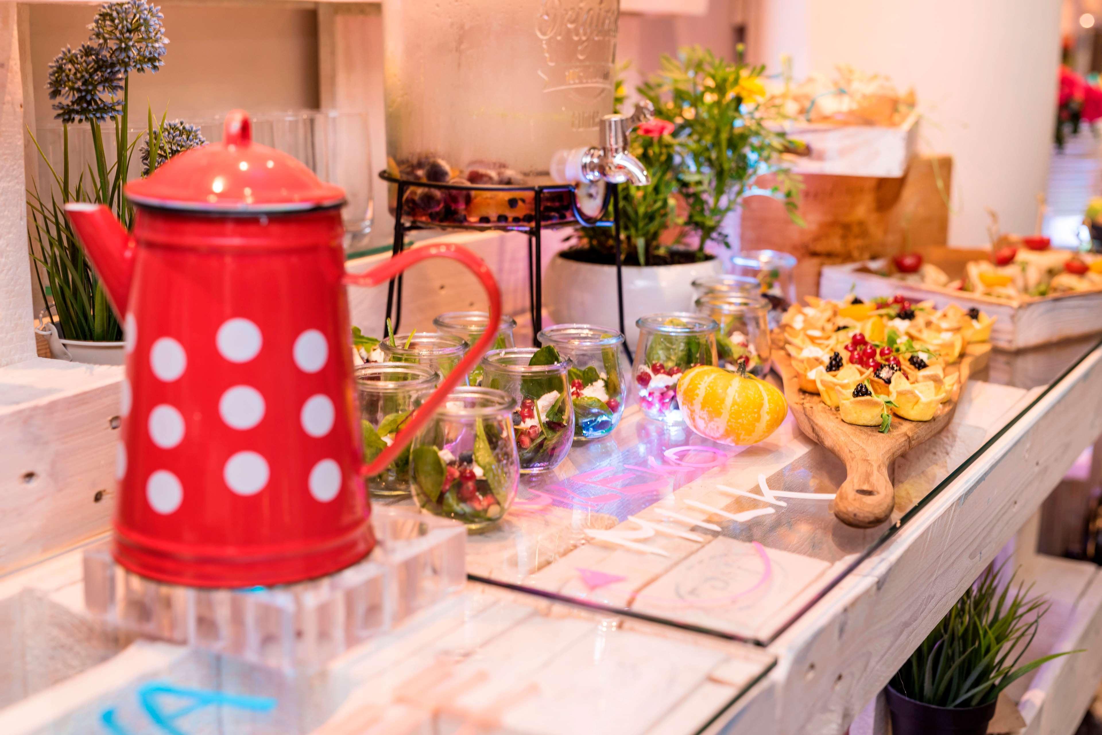 Radisson Blu Hotel Krakow Exterior photo The photo displays a colorful food and drink setup. Prominently featured is a red kettle with white polka dots, placed on a clear stand. Surrounding the kettle are glass jars filled with vibrant greenery, possibly salads or herbal arrangements. There