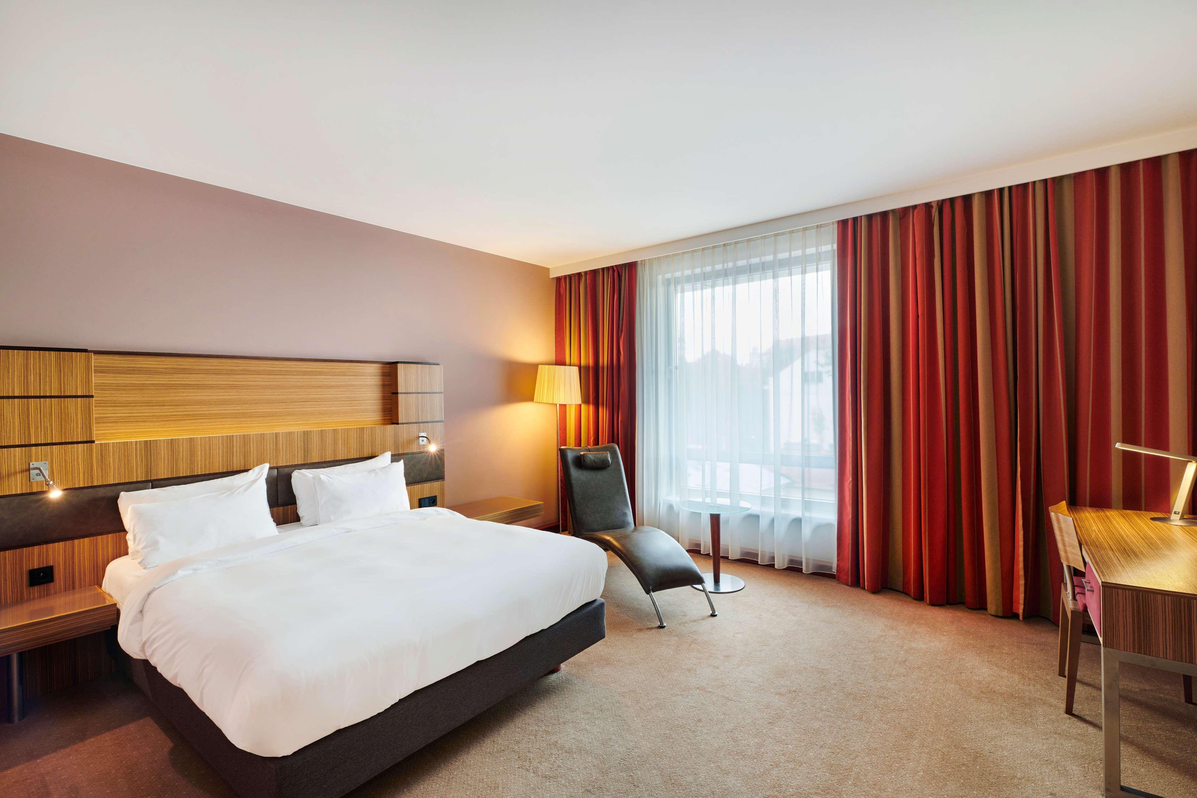 Radisson Blu Hotel Krakow Exterior photo The photo shows a modern hotel room featuring a large bed with white bedding and two pillows. The walls are painted in a warm tone, and there's a stylish wooden headboard. Next to the bed, there's an elegant lamp providing soft lighting. A large wind