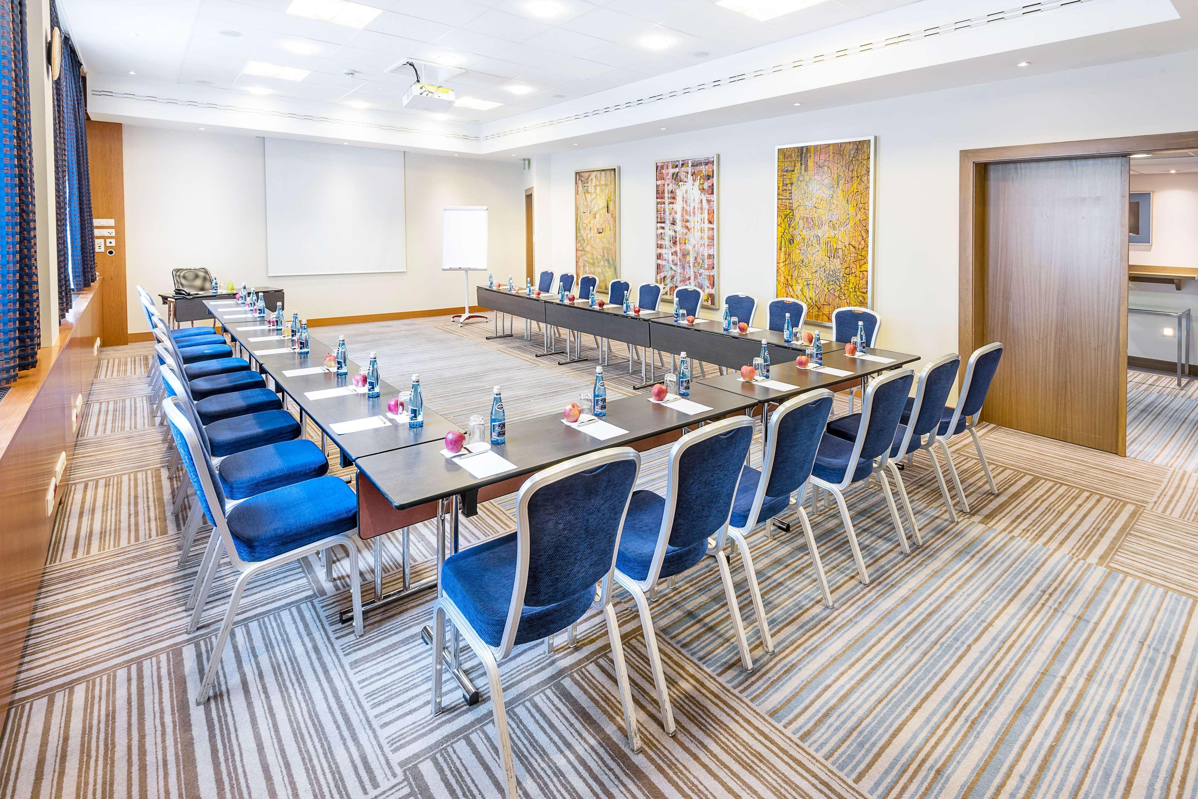 Radisson Blu Hotel Krakow Exterior photo The image shows a conference room set up for a meeting. There are several long tables arranged in a U-shape, with blue chairs placed around them. Each chair has a small water bottle on the table, along with some stationery items, likely for the atten