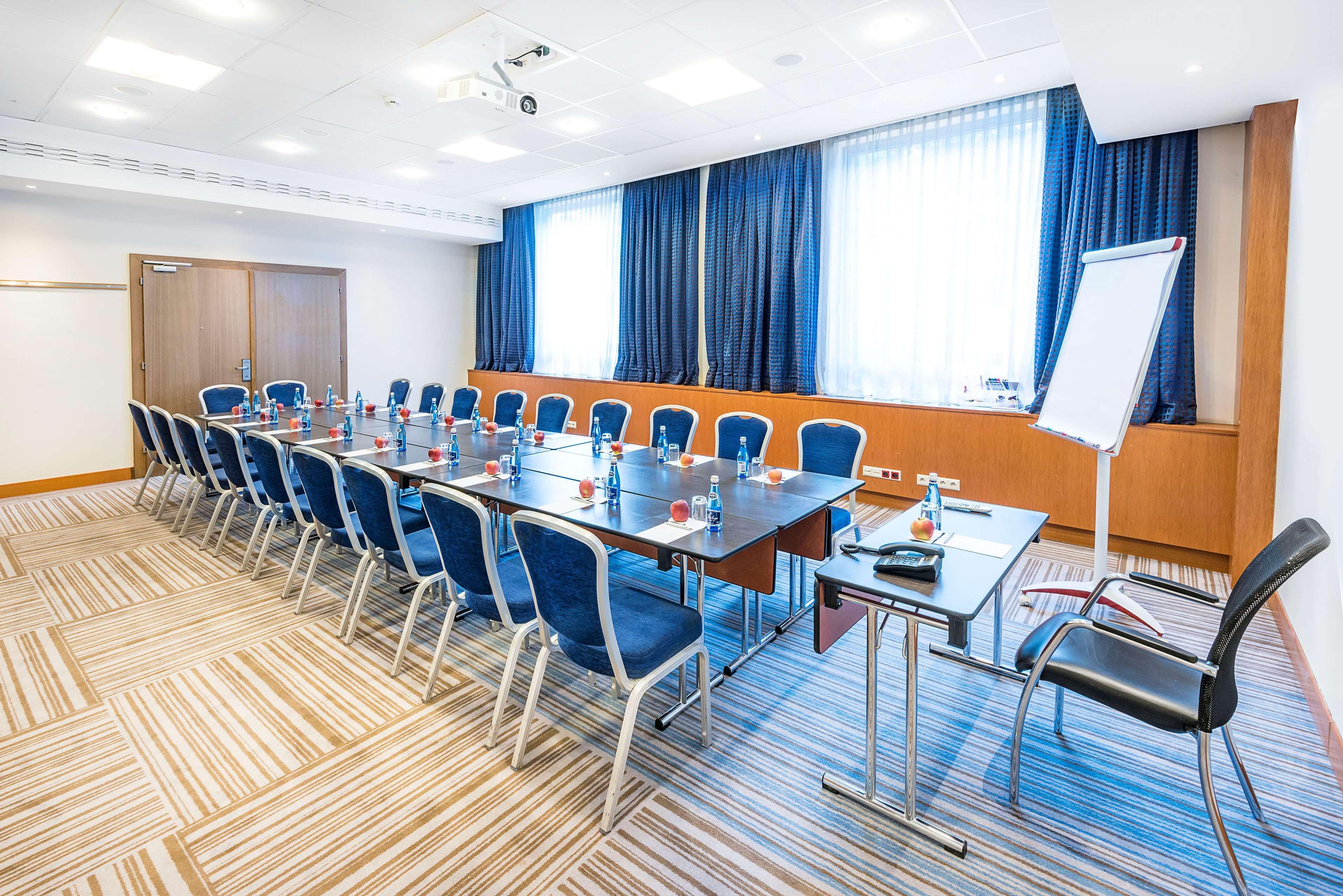 Radisson Blu Hotel Krakow Exterior photo The photo shows a conference room set up for a meeting. There are several rows of blue chairs arranged around a long rectangular table. The table is equipped with small bottles of water, and there appears to be a flip chart or whiteboard on one side 