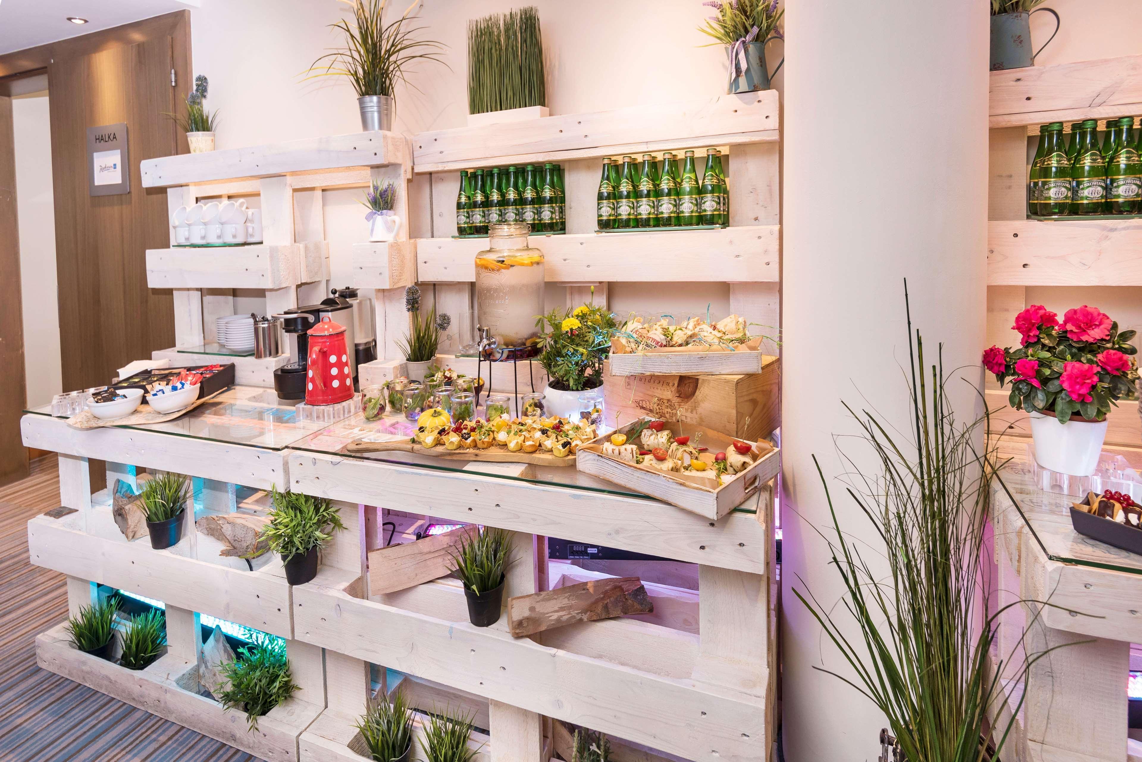 Radisson Blu Hotel Krakow Exterior photo The photo shows a stylish buffet or food display area made from wooden pallets. It features various food items, including pastries and small dishes, arranged neatly on the shelves. There are decorative elements like potted plants and artificial grass