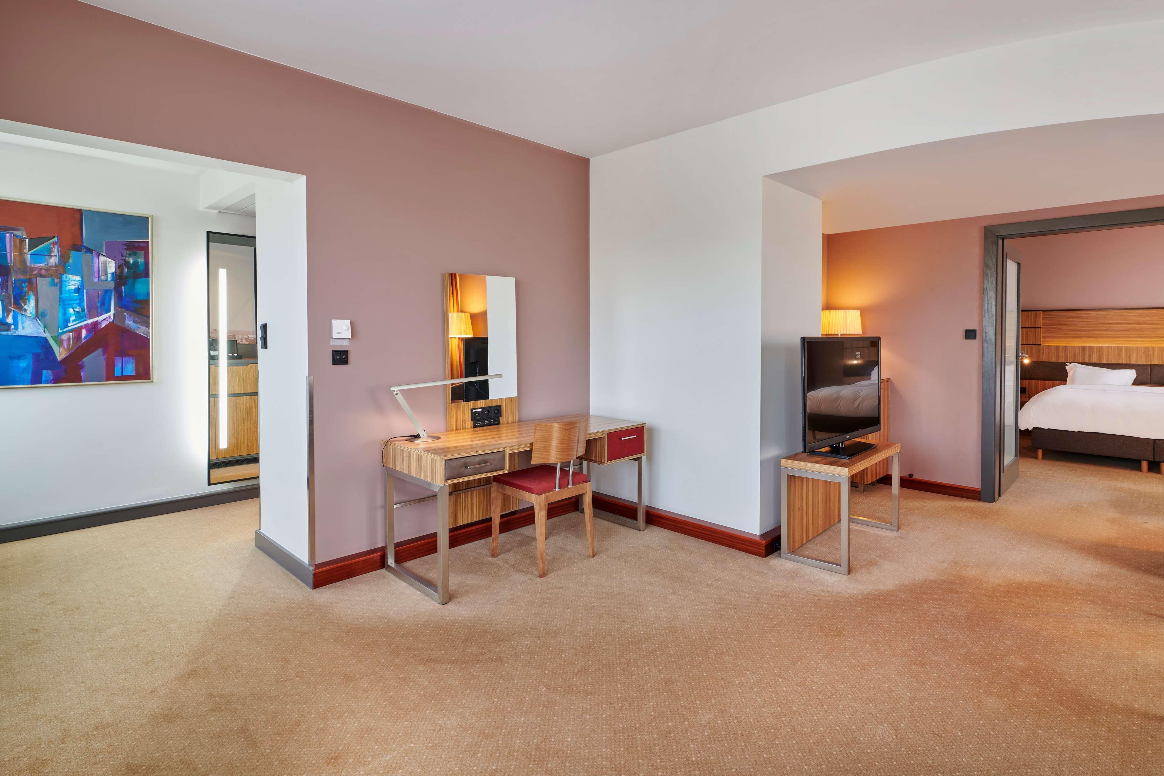 Radisson Blu Hotel Krakow Exterior photo The photo shows a spacious hotel room or suite. On one side, there's a vanity desk with a mirror and a small drawer. The walls are painted in a soft pink color, creating a warm atmosphere. In the background, there is a doorway leading to another area
