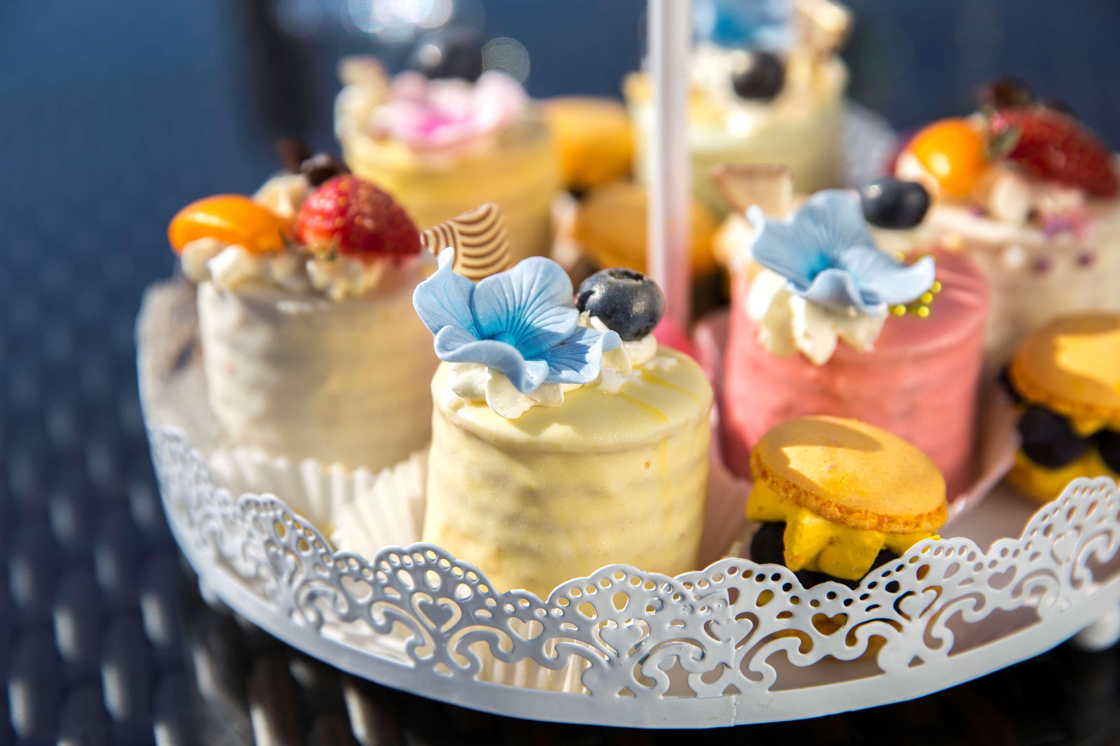 Radisson Blu Hotel Krakow Exterior photo The photo shows a decorative platter filled with small, colorful cakes or pastries. Each cake is topped with various decorations, including edible flowers, fruits, and cream. The cakes appear to be in different shades, such as yellow, pink, and white