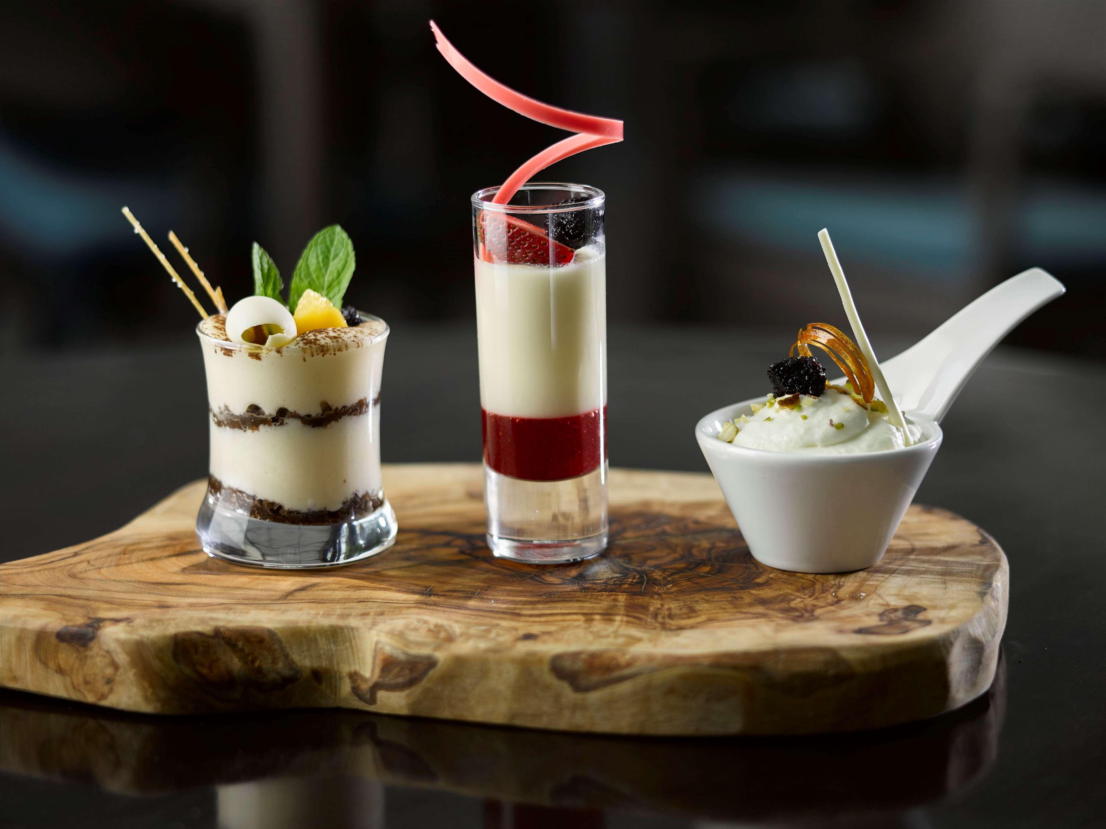 Radisson Blu Hotel Krakow Exterior photo The photo features a platter with three distinct desserts, elegantly presented on a wooden board:

1. **First Dessert**: A glass dessert with layers of cream and chocolate, topped with small fruits and adorned with mint leaves and decorative sticks.
