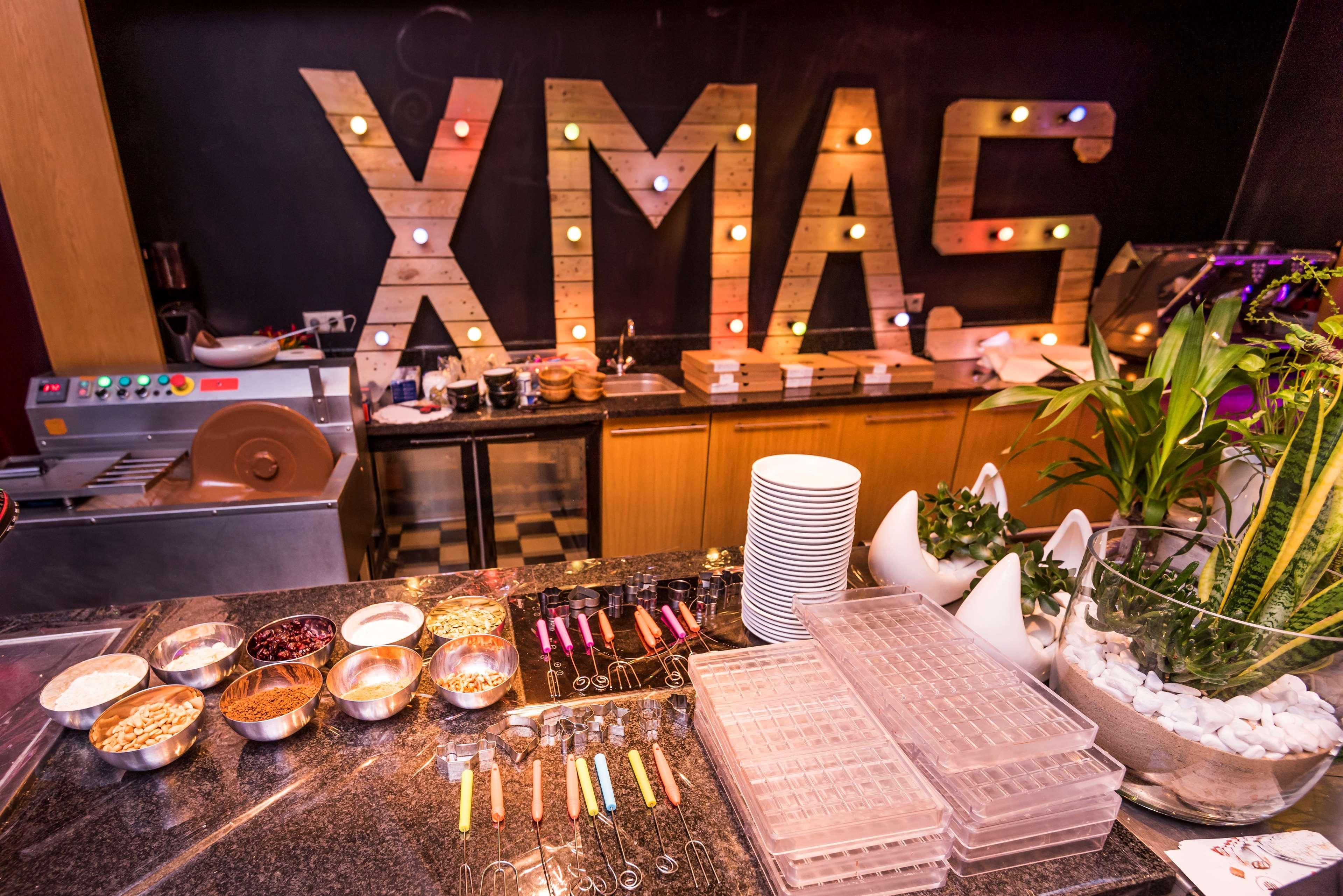 Radisson Blu Hotel Krakow Exterior photo The photo shows a festive setting with a prominent display featuring the word "XMAS" made of wooden letters illuminated by colorful lights. In the foreground, there's a buffet-style table set up, displaying various bowls containing food items, possib
