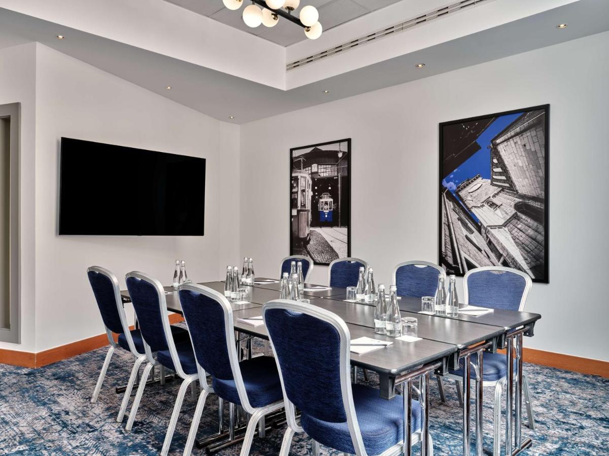 Radisson Blu Hotel Krakow Exterior photo The photo depicts a modern conference room. It features a long rectangular table with several blue upholstered chairs arranged around it. On the table are glass water bottles and glasses, suggesting a setup for a meeting or presentation. The room has