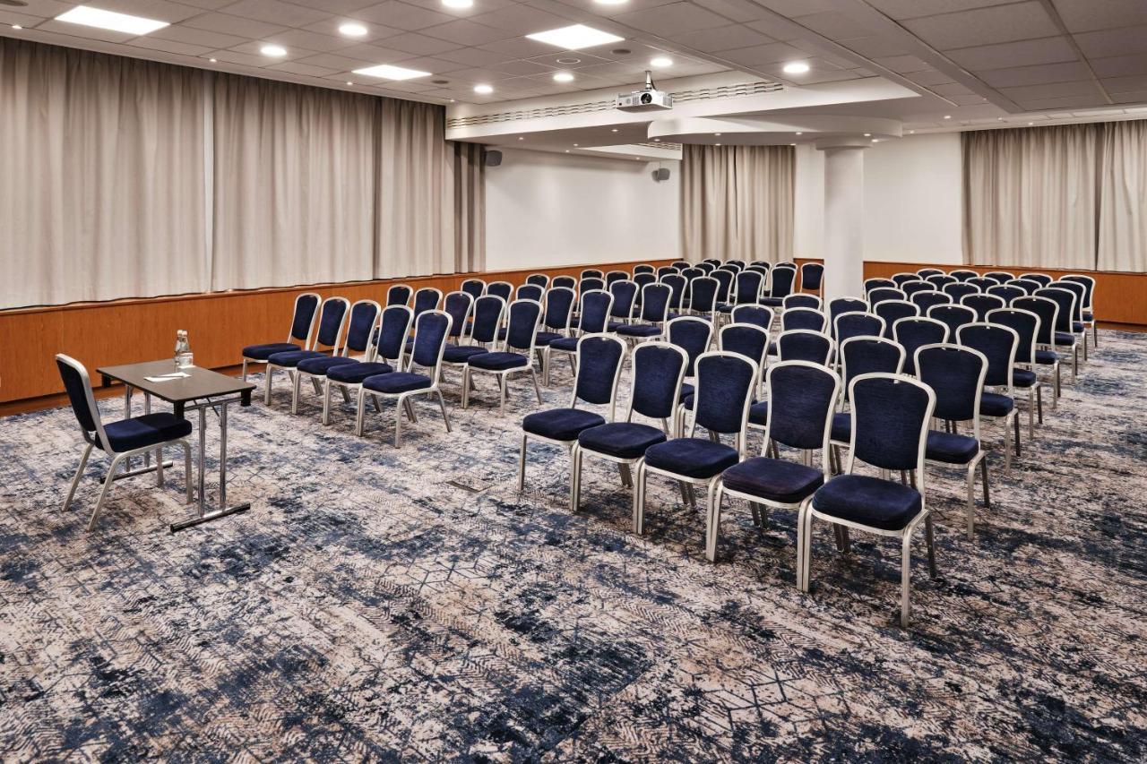Radisson Blu Hotel Krakow Exterior photo The photo shows a conference room set up for a meeting or event. There are rows of blue chairs arranged neatly, indicating a capacity for attendees. At the front of the room, there is a small table, likely for speakers or presenters, alongside a wate