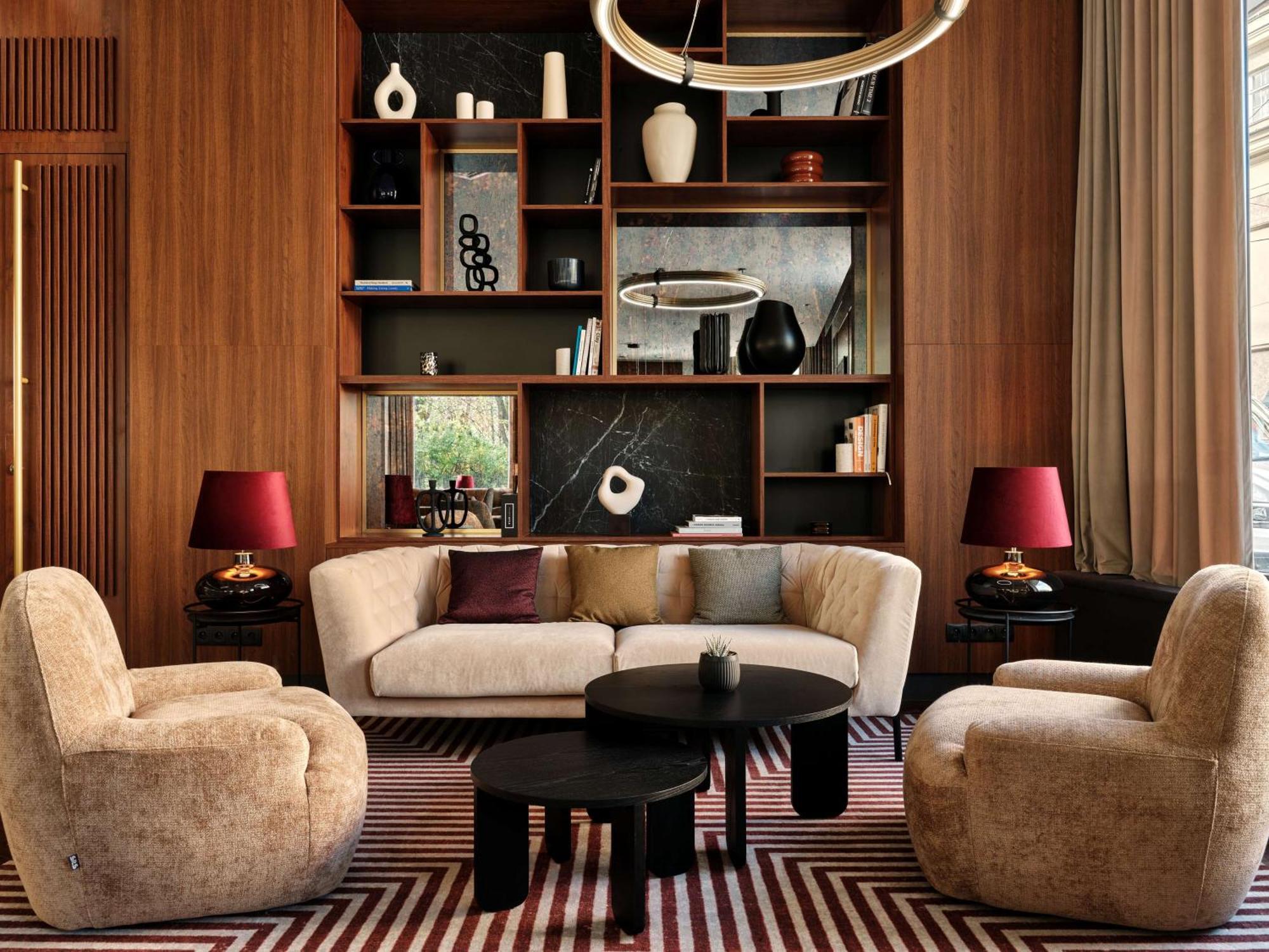 Radisson Blu Hotel Krakow Exterior photo The image shows a stylish and modern living room space. It features a curved beige sofa centered in the room, accompanied by a round black coffee table. There are two plush armchairs in a similar beige tone positioned across from the sofa. Behind the