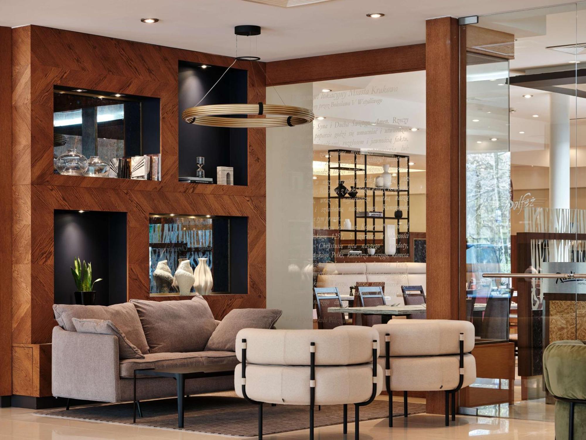 Radisson Blu Hotel Krakow Exterior photo The photo displays a modern and stylish interior setting, likely from a hotel lobby or a chic lounge area. It features a seating arrangement consisting of a plush gray sofa and two unique chairs that blend comfort and contemporary design. Behind the 