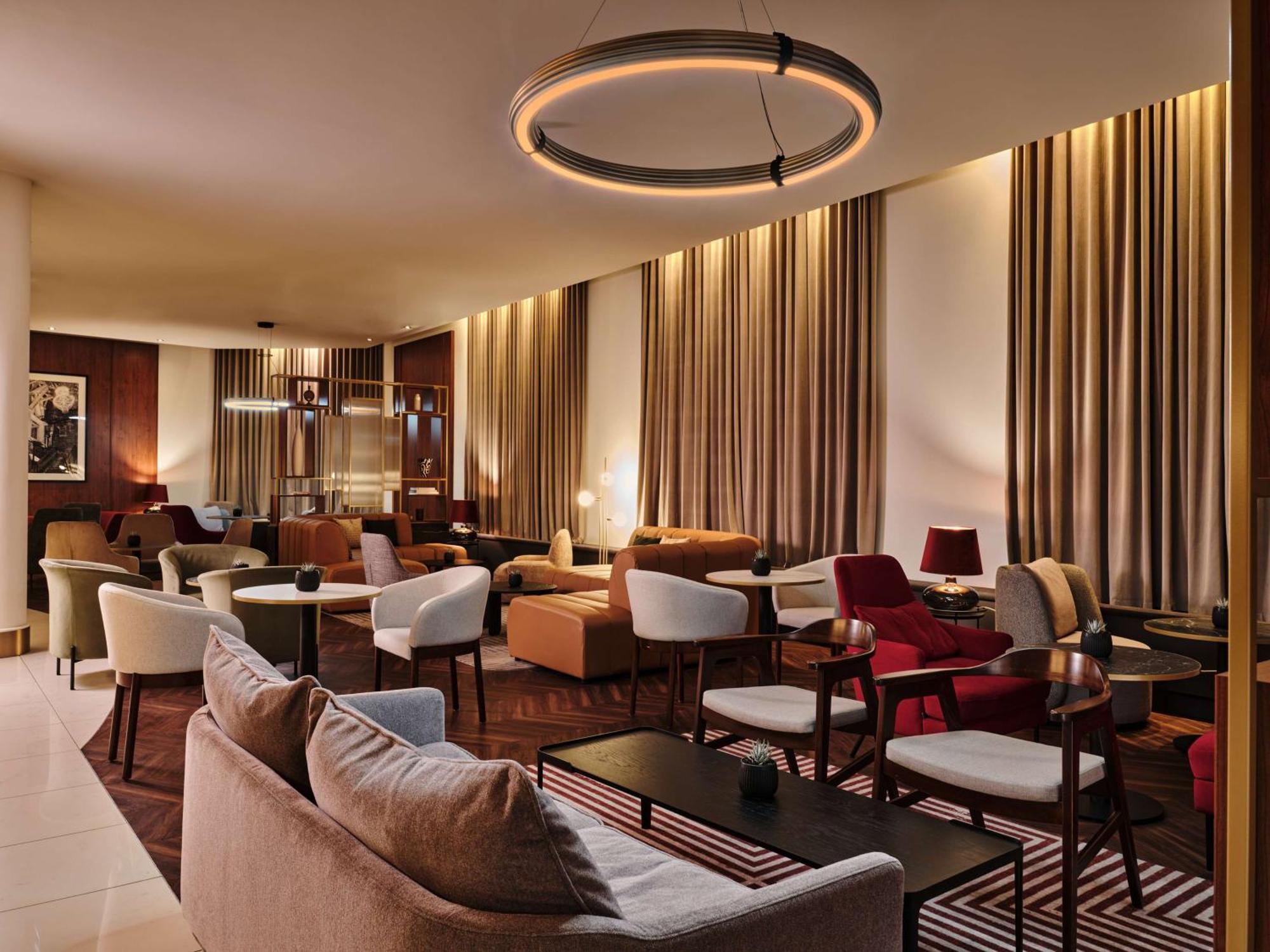 Radisson Blu Hotel Krakow Exterior photo The photo depicts a modern, stylish lounge area with warm lighting. The space features various seating arrangements, including comfortable sofas and armchairs in different colors and styles. There are elegant tables placed throughout the area, creati