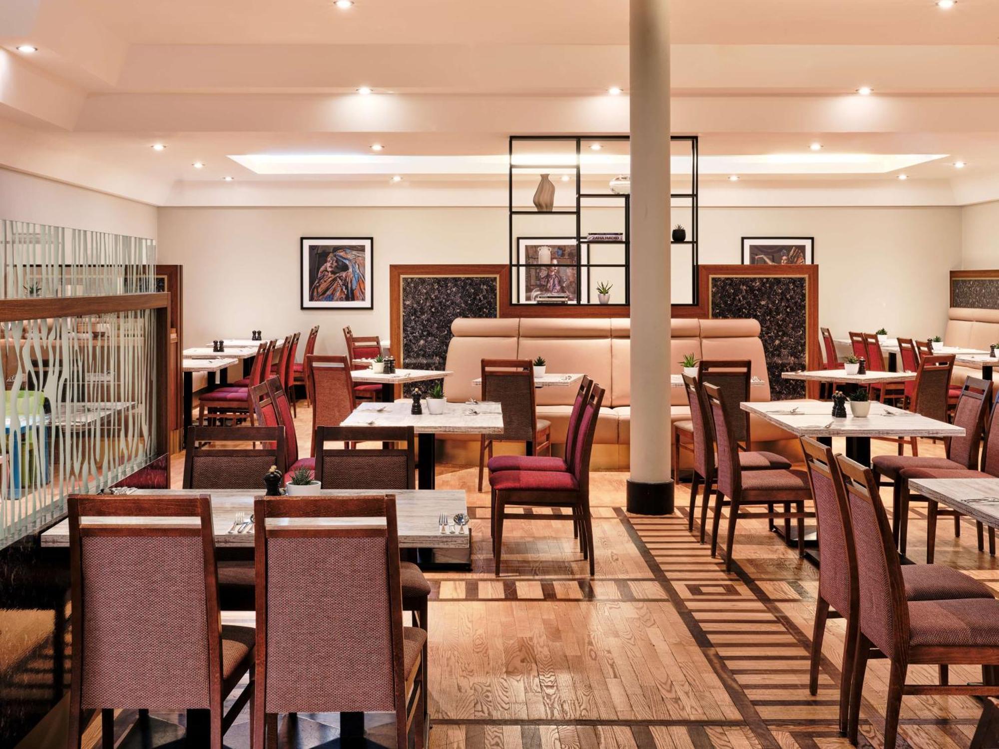 Radisson Blu Hotel Krakow Exterior photo The photo shows a spacious and modern restaurant interior. There are several tables arranged with chairs, featuring a combination of wooden and fabric elements. The design is elegant, with soft lighting and a neutral color palette. The decor includes