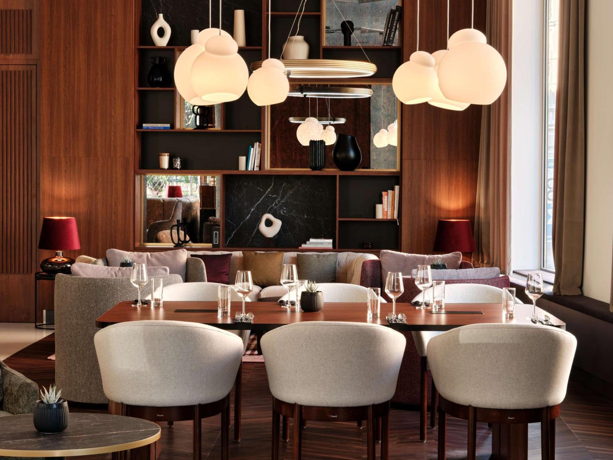 Radisson Blu Hotel Krakow Exterior photo The photo depicts a stylish and modern dining area. The interior features a sleek wooden wall with built-in shelves displaying decor items and books. The lighting is soft, provided by unique cloud-shaped pendant lights hanging from the ceiling. 

In 