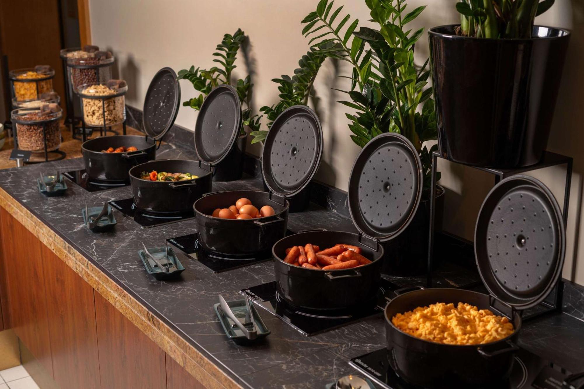 Radisson Blu Hotel Krakow Exterior photo The photo shows a buffet setup with several black cooking pots arranged in a row on a dark countertop. Each pot is covered with a lid, and some pots are filled with various prepared foods. The dishes visible include eggs, hot dogs, macaroni and chees