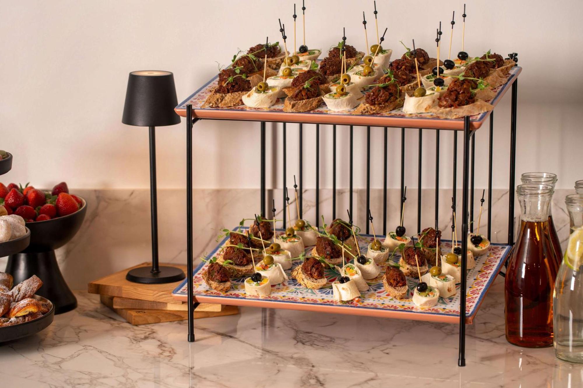 Radisson Blu Hotel Krakow Exterior photo The image shows a two-tier serving display filled with appetizers. The top and bottom layers feature an assortment of bite-sized food items, likely a mixture of meat and vegetables, artfully presented with decorative toothpicks or skewers. The displa
