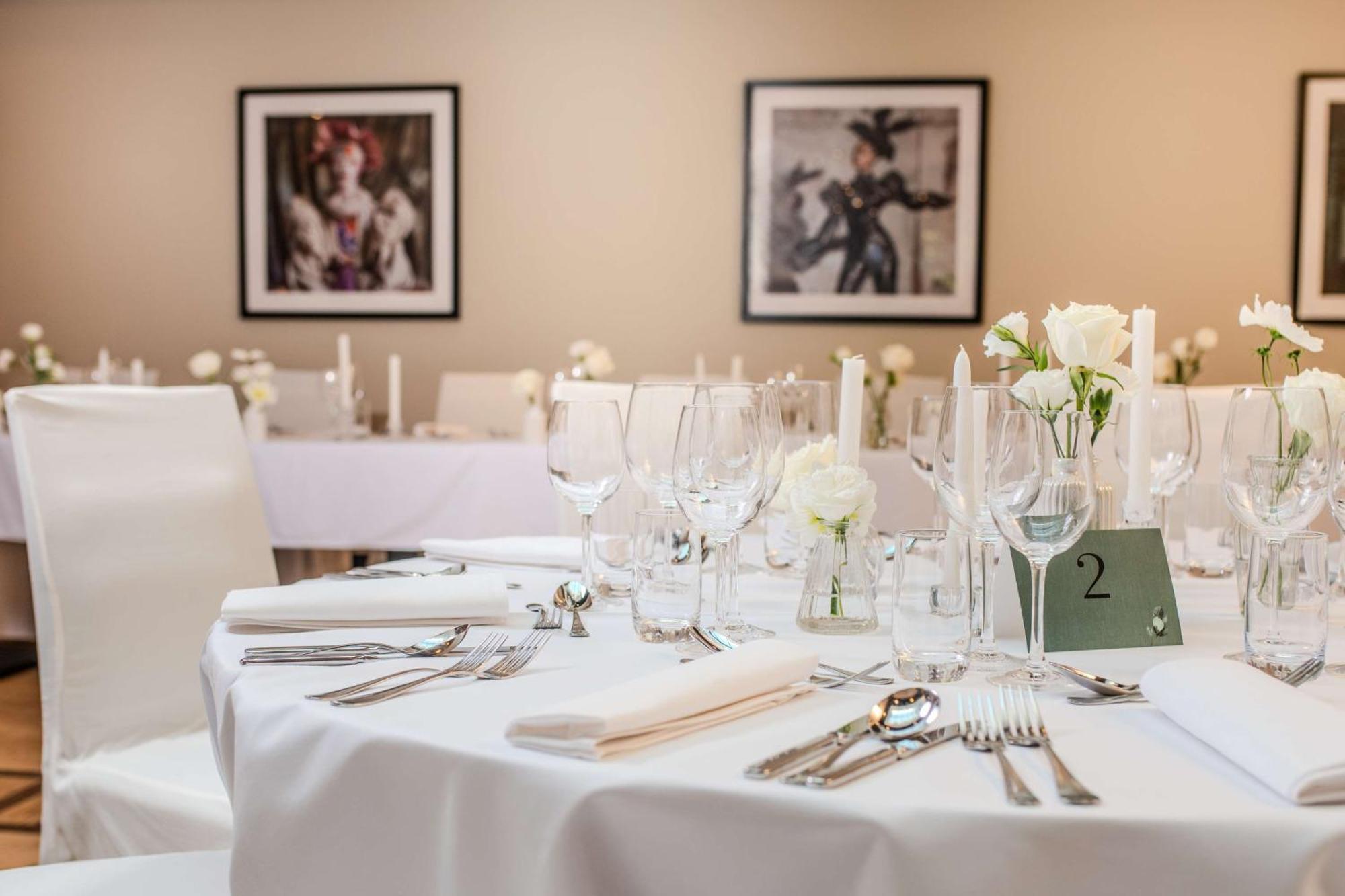Radisson Blu Hotel Krakow Exterior photo The photo shows a well-set dining table in a banquet or event space. The table is covered with a white tablecloth and is elegantly arranged with various glassware, including wine glasses and water glasses, alongside neatly placed cutlery. There are s